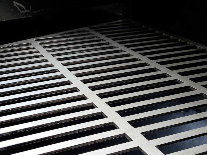 Laser cut stainless steel cooking grates shown inside of an offset smoker
